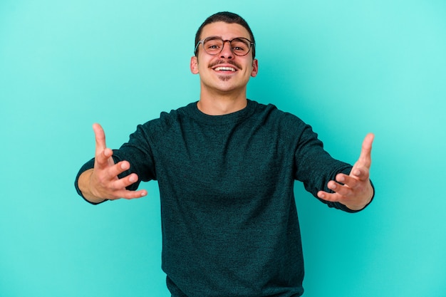 Young caucasian man on blue showing a welcome expression.