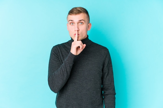 Photo young caucasian man on a blue wall keeping a secret or asking for silence.