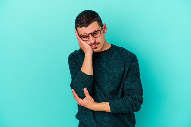 Young caucasian man on blue who is bored, fatigued and need a relax day.