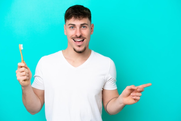 Young caucasian man brushing teeth isolated on blue background surprised and pointing finger to the side