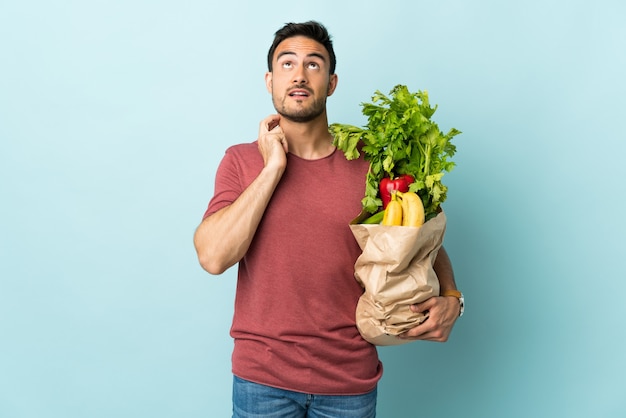 アイデアを考えて青い壁に分離された野菜を買う白人の若い男