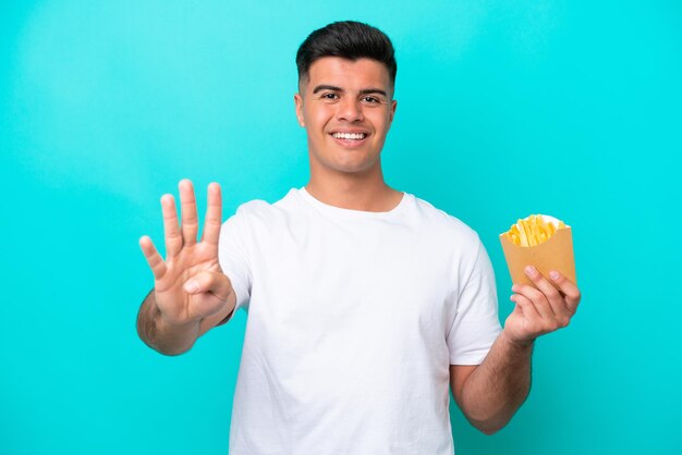 Young caucasian man catching french fries isolated on blue background happy and counting four with fingers