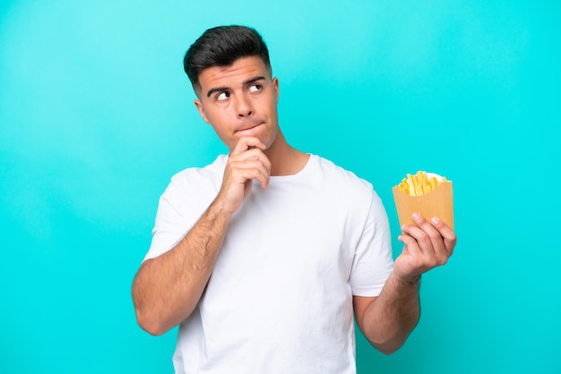 疑問と思考を持っている青い背景に分離されたフライドポテトをキャッチする若い白人男性