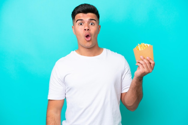 Young caucasian man catching french fries isolated on blue background looking up and with surprised expression