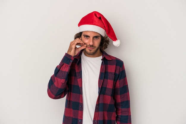 Young caucasian man celebrating Christmas isolated on gray background with fingers on lips keeping a secret.