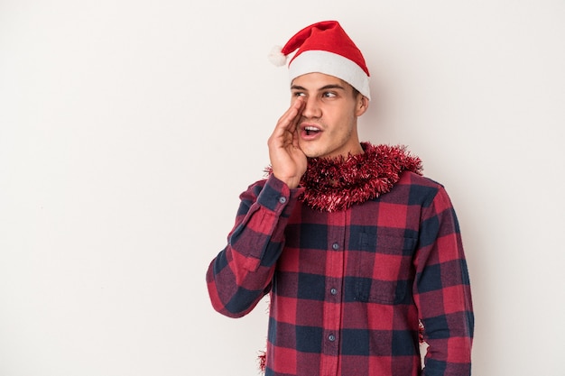 Young caucasian man celebrating Christmas isolated on white background is saying a secret hot braking news and looking aside