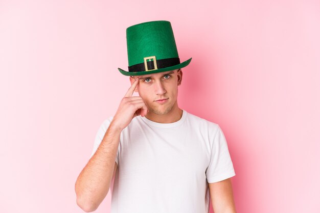 Young caucasian man celebrating saint patricks day pointing temple with finger, thinking, focused on a task.