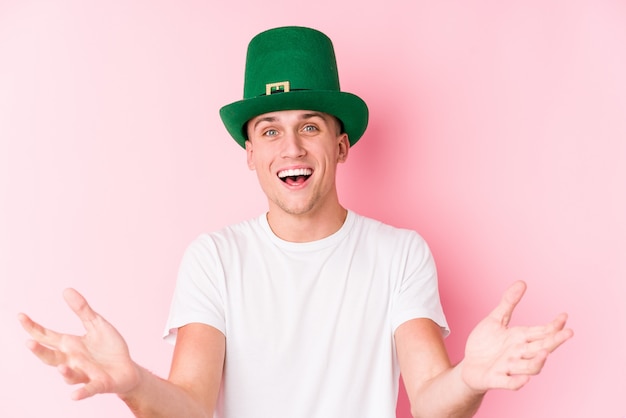 Young caucasian man celebrating saint patricks day receiving a pleasant surprise, excited and raising hands.