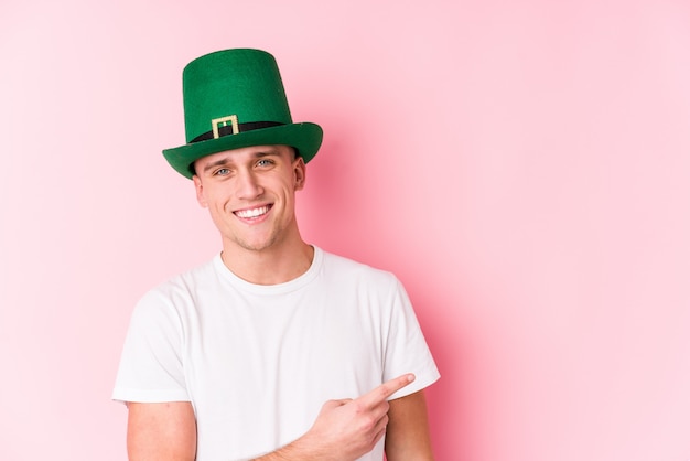 Young caucasian man celebrating saint patricks day smiling and pointing aside, showing something at blank space.