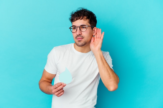 Young caucasian man celebrating world water day isolated trying to listening a gossip.