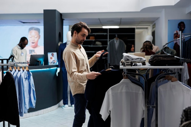 Young caucasian man checking tie and shirt match while choosing formal outfit in clothing store. Customer examining apparel and accessory style while shopping for menswear in boutique