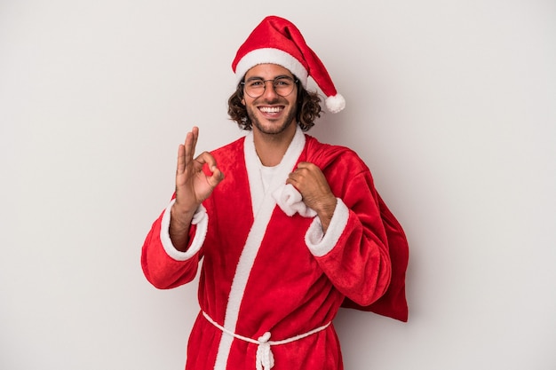 Молодой кавказский человек, замаскированный под Санта-Клауса, изолирован на сером фоне, веселый и уверенный, показывая хорошо жест.