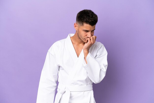 Young caucasian man doing karate isolated on purple background having doubts