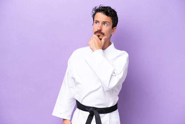 Young caucasian man doing karate isolated on purple background having doubts