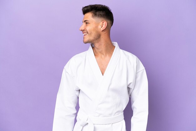 Young caucasian man doing karate isolated on purple background looking side