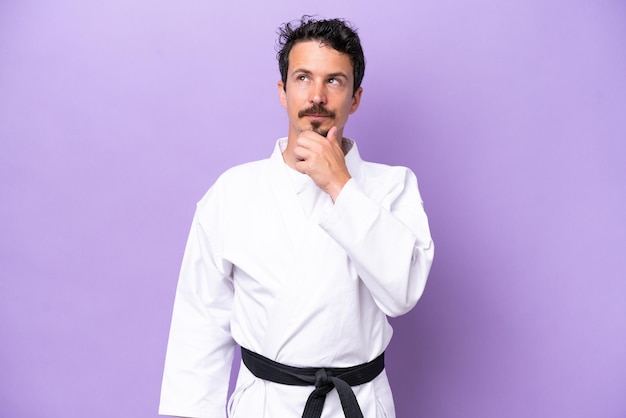 Young caucasian man doing karate isolated on purple background and looking up