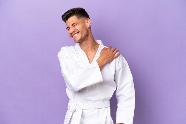 Young caucasian man doing karate isolated on purple background suffering from pain in shoulder for having made an effort