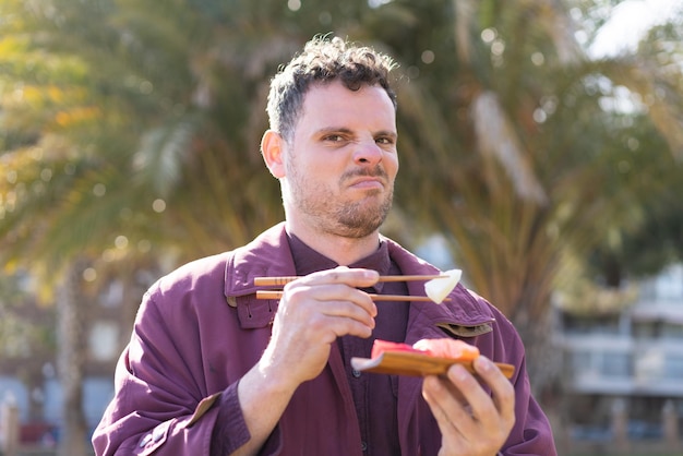 Young caucasian man eating sashimi at outdoors