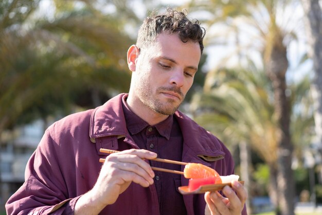 Young caucasian man eating sashimi at outdoors