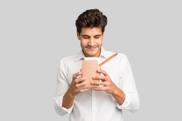 Young caucasian man eating a takeaway noodles isolated