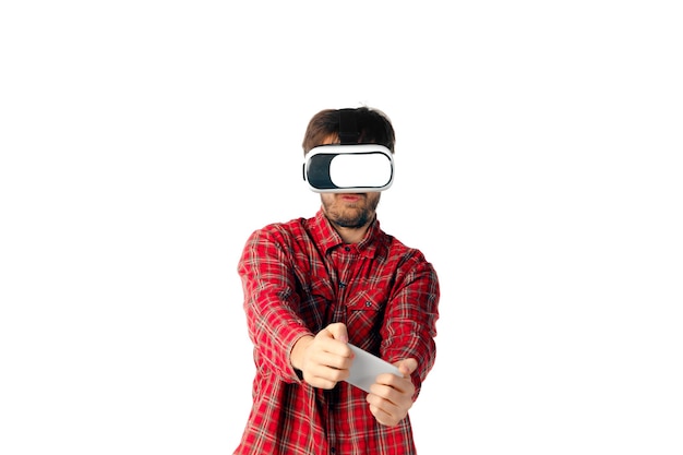 Young caucasian man emotional playing, using virtual reality headset and smartphone isolated.