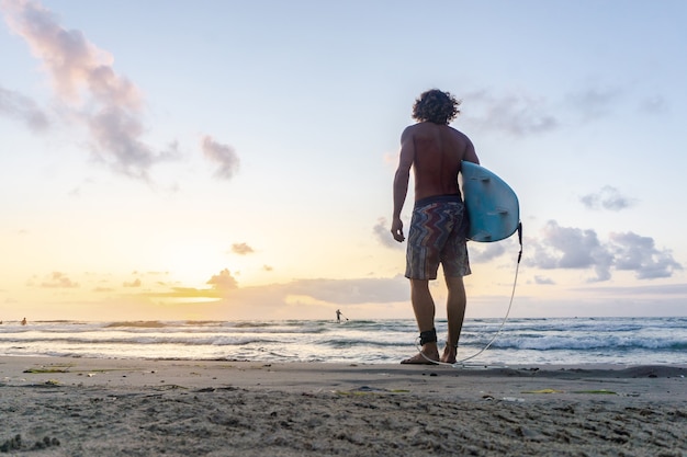 若い白人男性は日の出でサーフィンをすることに早く起きます