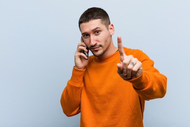 Фото Молодой кавказский человек держа телефон показывая номер один с пальцем.