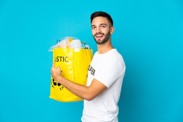 Young caucasian man holding a bag full of plastic bottles to\
recycle isolated