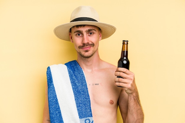 黄色の背景で隔離のビールを保持している若い白人男性