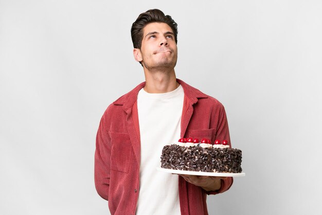 Young caucasian man holding birthday cake over isolated background and looking up