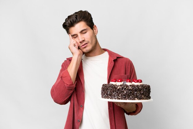 Young caucasian man holding birthday cake over isolated background with headache
