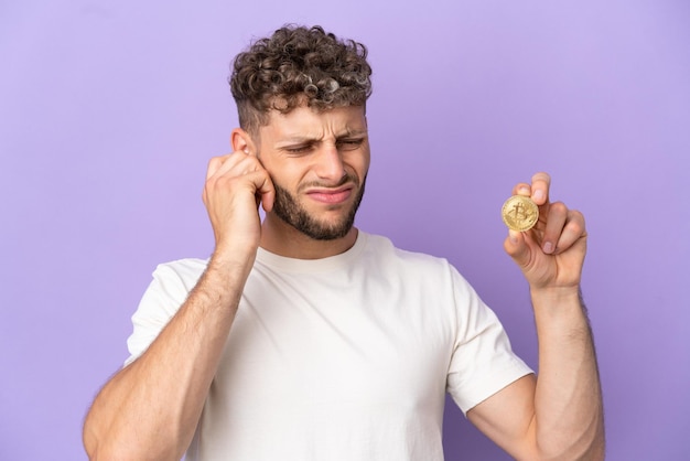 Young caucasian man holding a Bitcoin isolated on purple background frustrated and covering ears