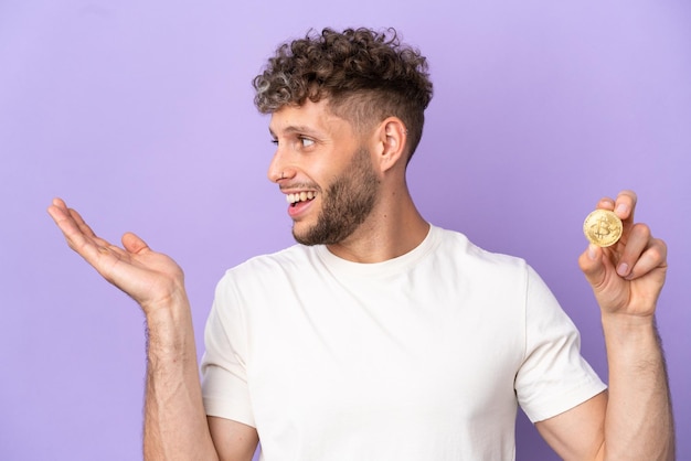 Young caucasian man holding a bitcoin isolated on purple background with surprise expression while looking side