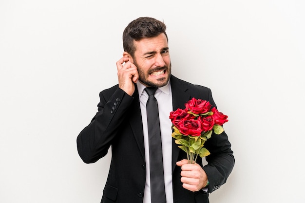 Young caucasian man holding a bouquet of flowers isolated on white background covering ears with hands