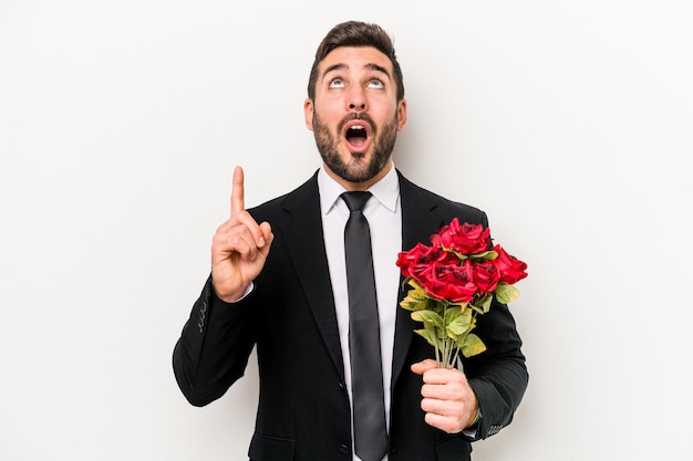 Young caucasian man holding a bouquet of flowers isolated on white background pointing upside with opened mouth