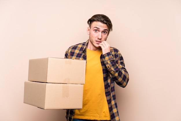 Young caucasian man holding boxes biting fingernails, nervous and very anxious.