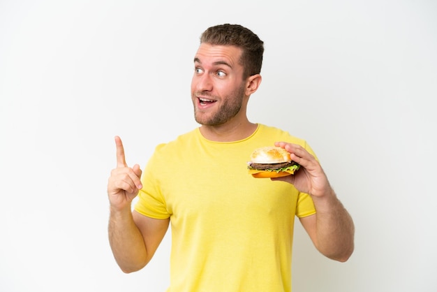 Young caucasian man holding a burger isolated on white background intending to realizes the solution while lifting a finger up