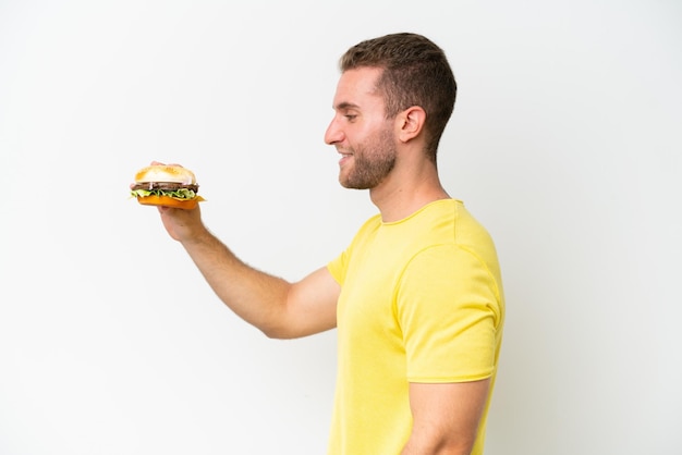 Young caucasian man holding a burger isolated on white background with happy expression
