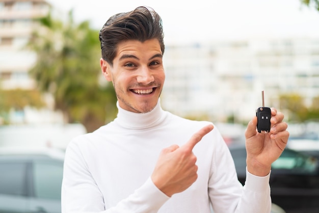 Young caucasian man holding car keys at outdoors and pointing it