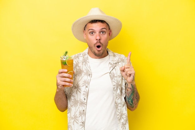 Young caucasian man holding a cocktail isolated on yellow background intending to realizes the solution while lifting a finger up