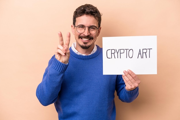 Young caucasian man holding a crypto art placard isolated on beige background showing number two with fingers.