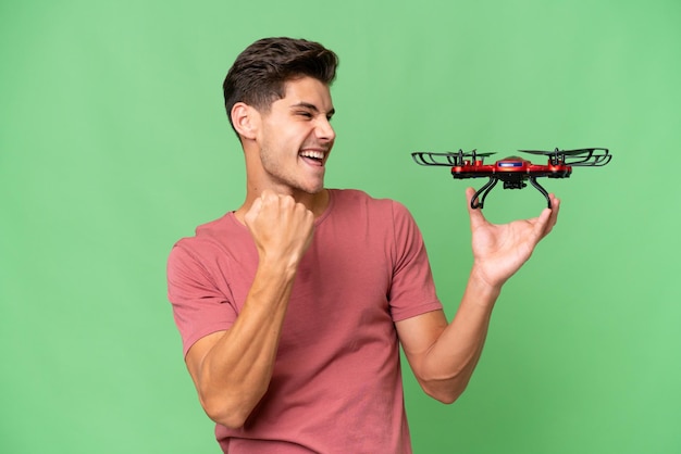 Young caucasian man holding a drone over isolated background celebrating a victory