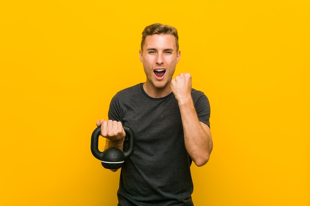 Young caucasian man holding a dumbbell cheering carefree and excited