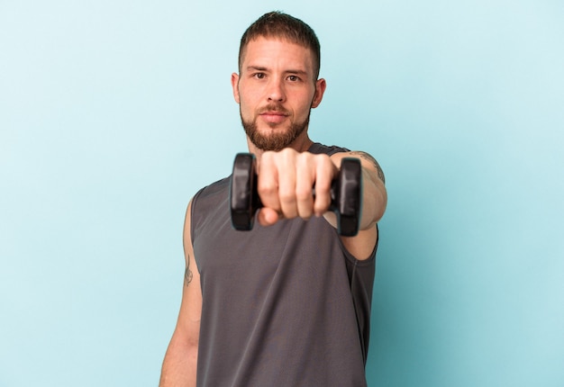 Young caucasian man holding dumbbell isolated on blue background