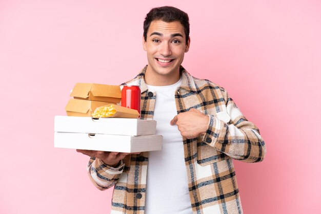 Young caucasian man holding fast food isolated on pink background with surprise facial expression