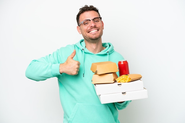 Young caucasian man holding fast food isolated on white background giving a thumbs up gesture