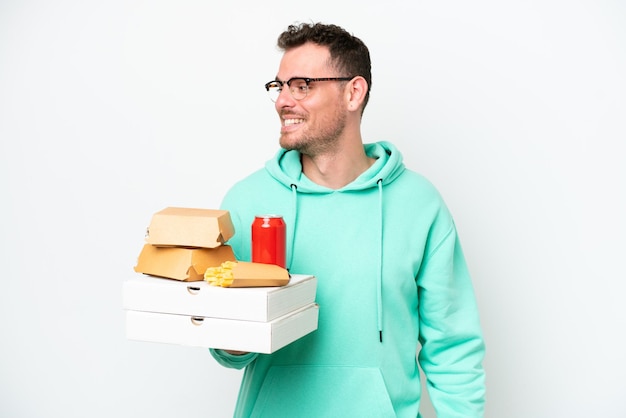 Young caucasian man holding fast food isolated on white background looking to the side and smiling