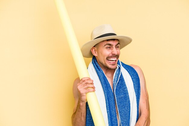 Young caucasian man holding a foam stick isolated on yellow background