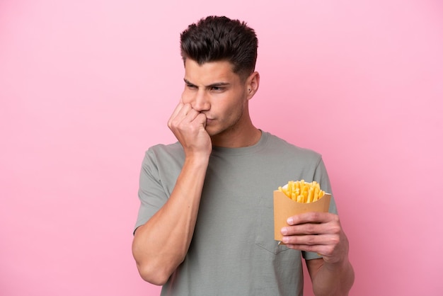 Young caucasian man holding fried chips isolated on pink background having doubts