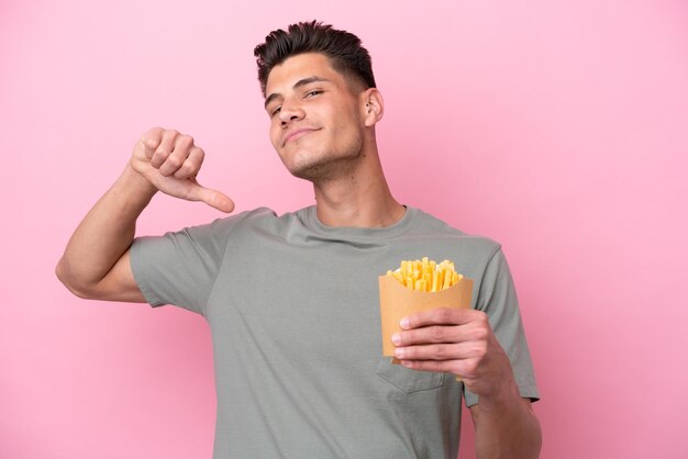 Young caucasian man holding fried chips isolated on pink background proud and selfsatisfied